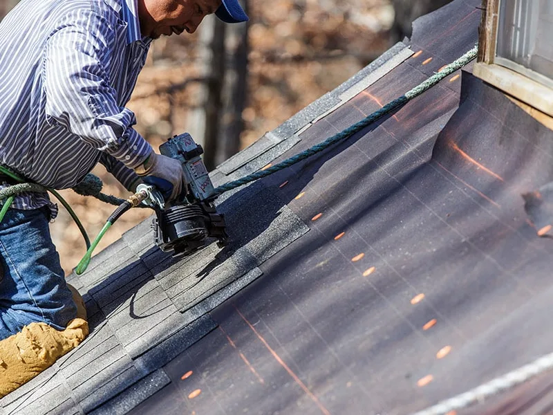 Worker on ladder cleaning gutters on brick residential home roof.